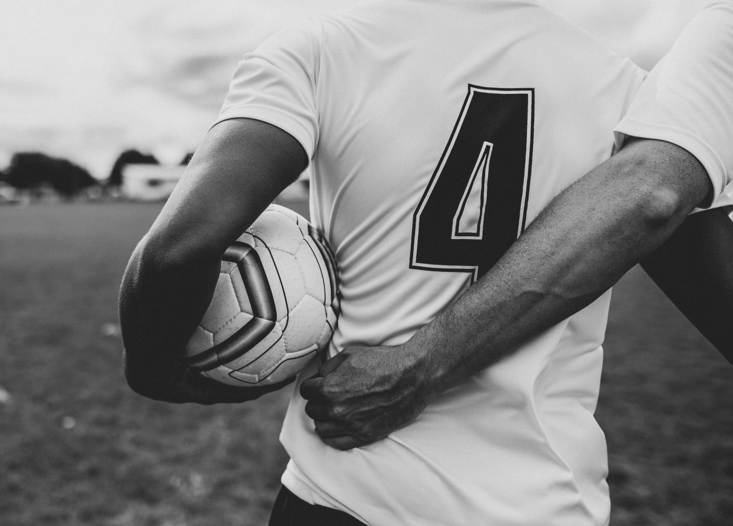 Black and white photo of athletes walking arm in arm with a soccer ball.